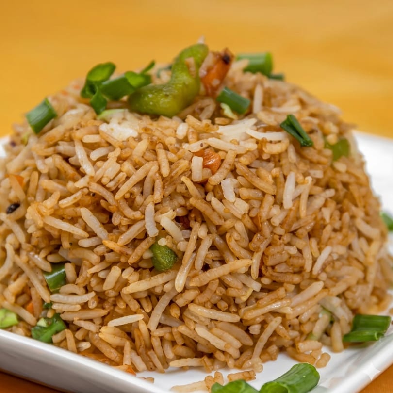 Close-up of a mound of fried rice with green onions and peppers on a white plate.