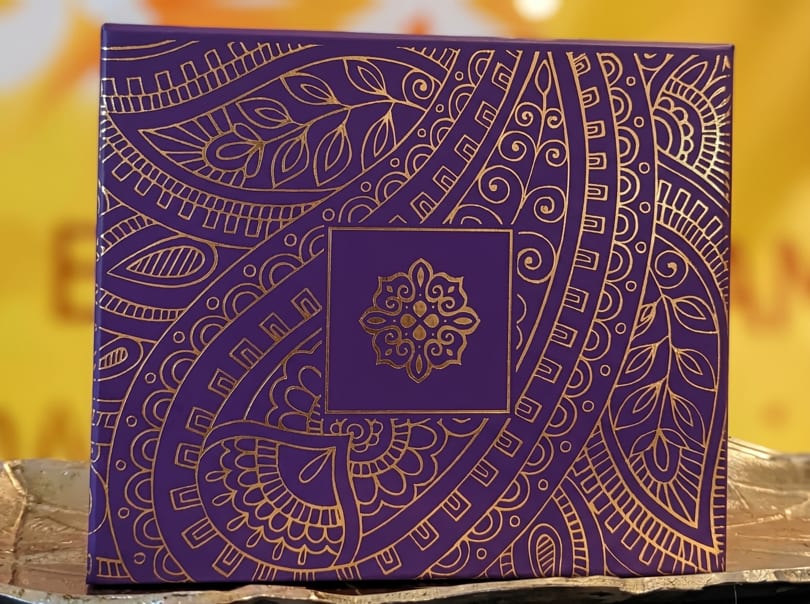 Purple box with intricate gold patterns and a central floral design, on a gold surface.