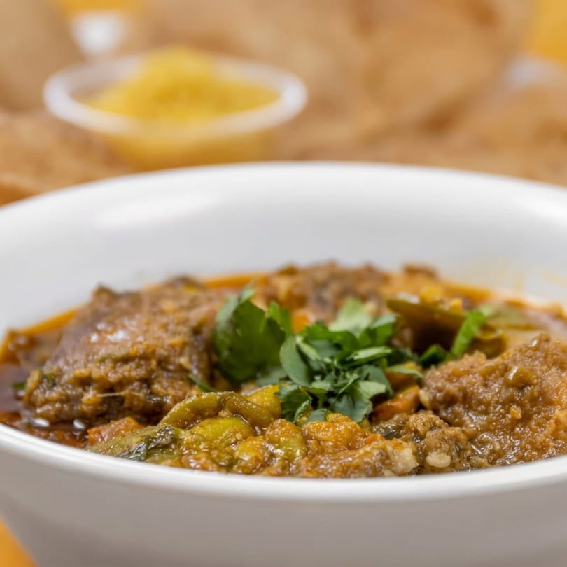 Close-up of a white bowl filled with a rich, savory stew, garnished with fresh cilantro.