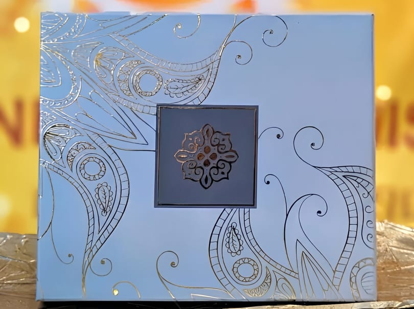 Light blue box with intricate gold and black designs, featuring a central gold medallion.