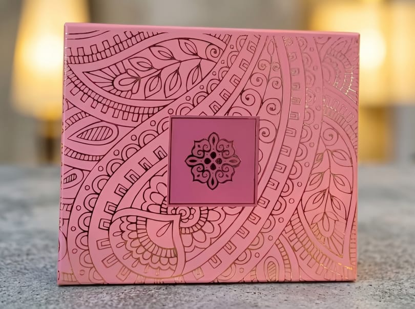 Pink box with intricate gold patterns and a dark pink square with a gold emblem.