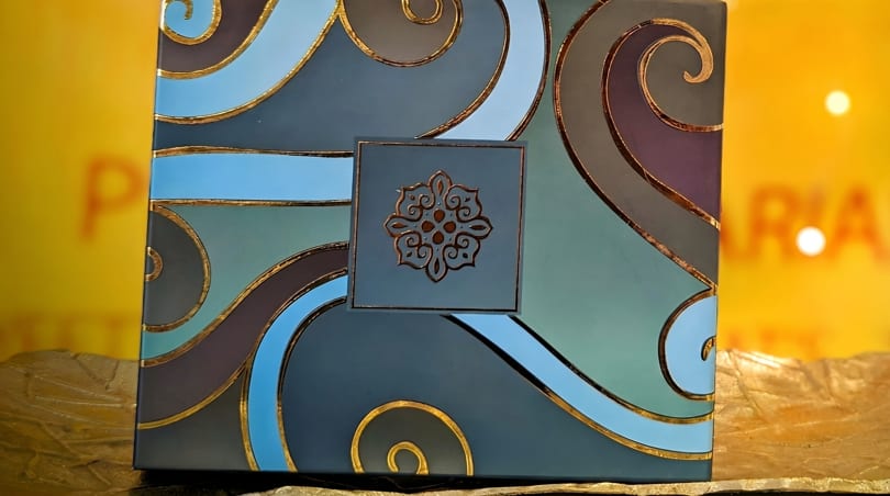 A decorative box with blue, teal, and purple waves outlined in gold, featuring a gold medallion.